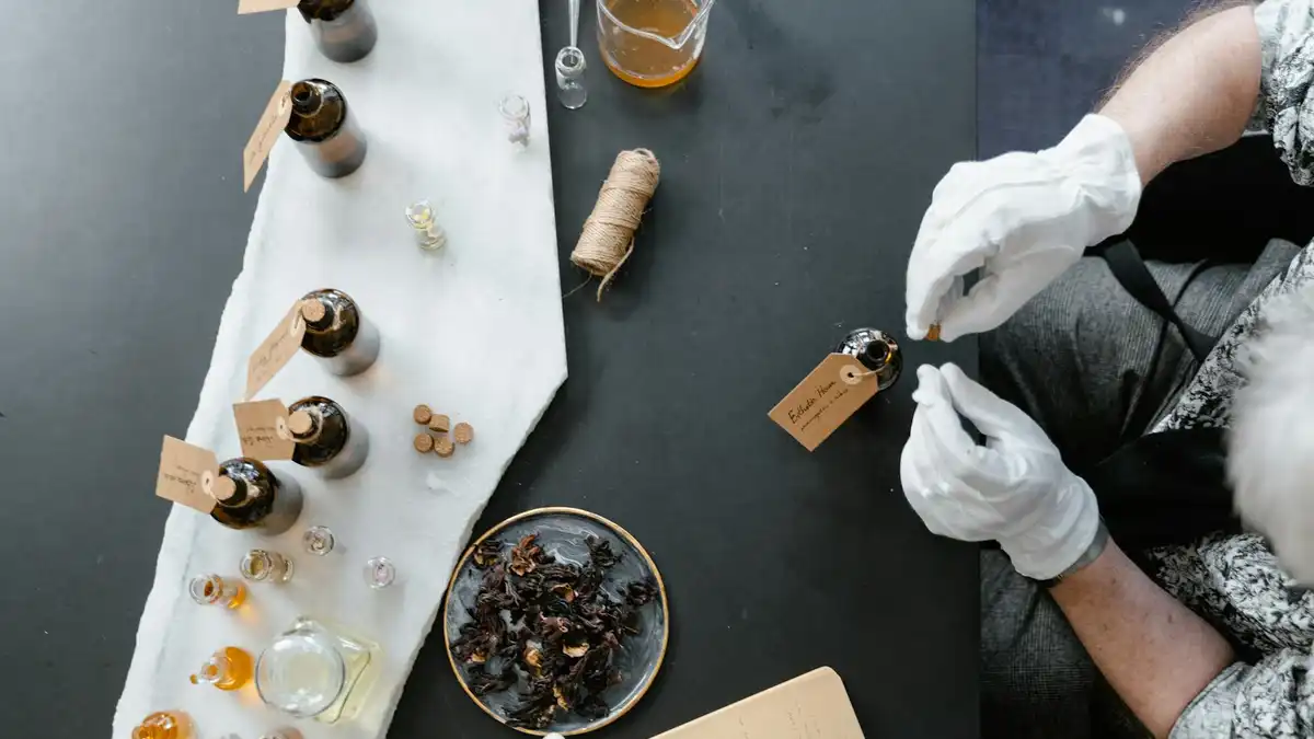 Mesa de perfumista com frascos de vidro, essências, ingredientes botânicos e caderno de anotações