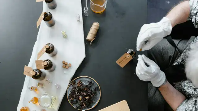 Mesa de perfumista com frascos de vidro, essências, ingredientes botânicos e caderno de anotações