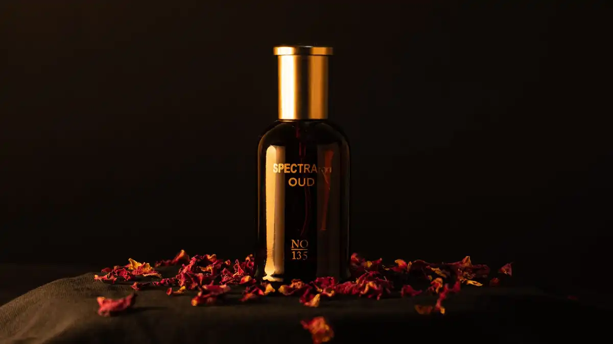 Frasco escuro de perfume oud com tampa dourada, cercado por pétalas de rosa sobre fundo escuro