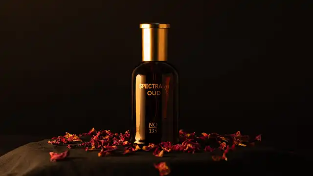 Frasco escuro de perfume oud com tampa dourada, cercado por pétalas de rosa sobre fundo escuro