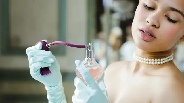Mulher elegante de luvas segurando um vaporizador de perfume vintage prestes a aplicá-lo