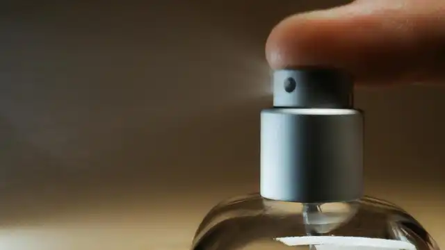 Close-up de uma pessoa borrifando um perfume de frasco com atomizador prateado, com névoa visível