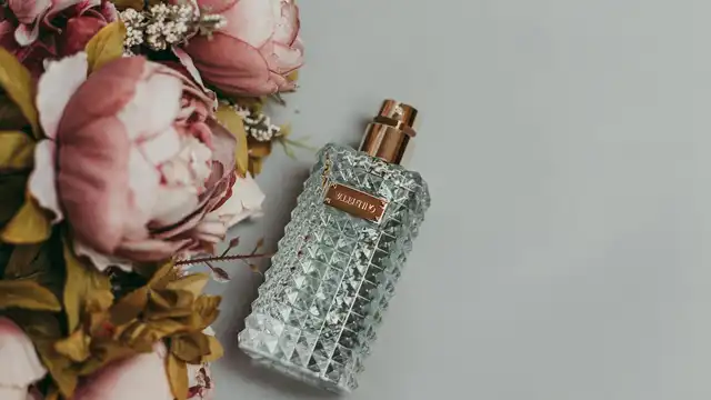 Frasco de perfume facetado ao lado de peônias cor-de-rosa, representando as notas florais de uma fragrância