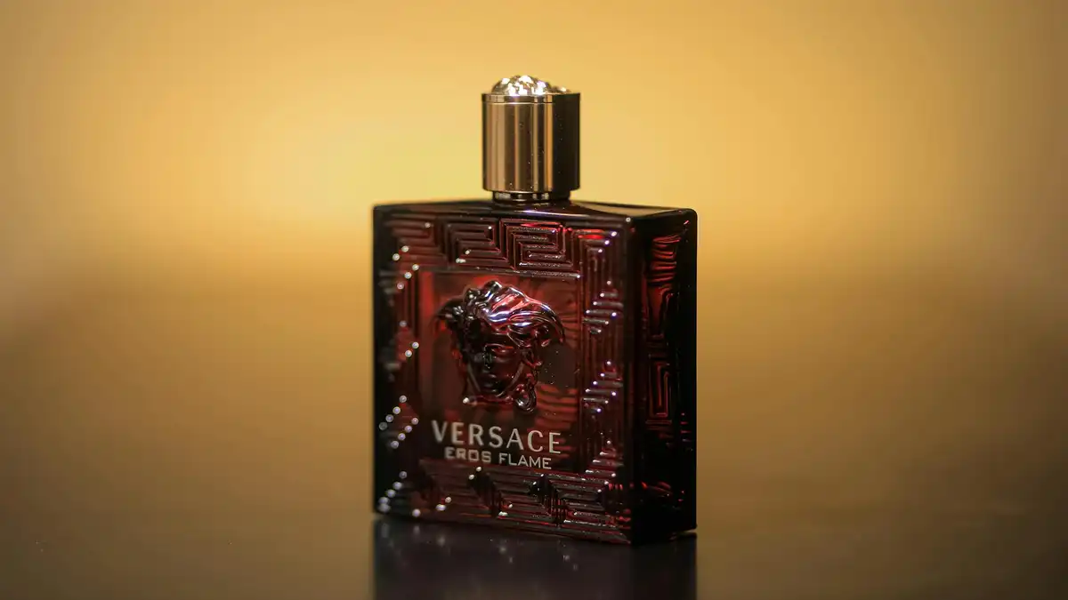 Frasco de perfume escuro sobre superfície reflexiva com fundo desfocado — representa fragrâncias modernas com base ambarada sintética