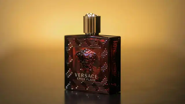 Frasco de perfume escuro sobre superfície reflexiva com fundo desfocado — representa fragrâncias modernas com base ambarada sintética
