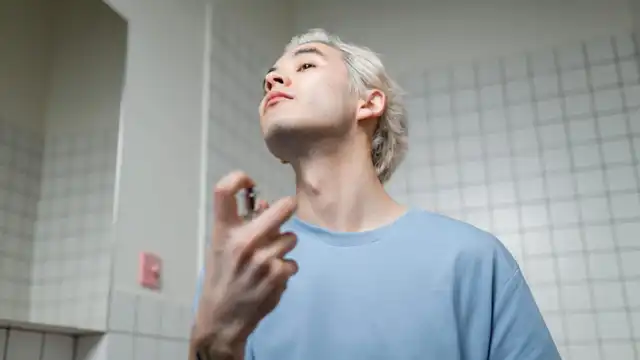 Pessoa aplicando perfume no pescoço com frasco spray em ambiente claro