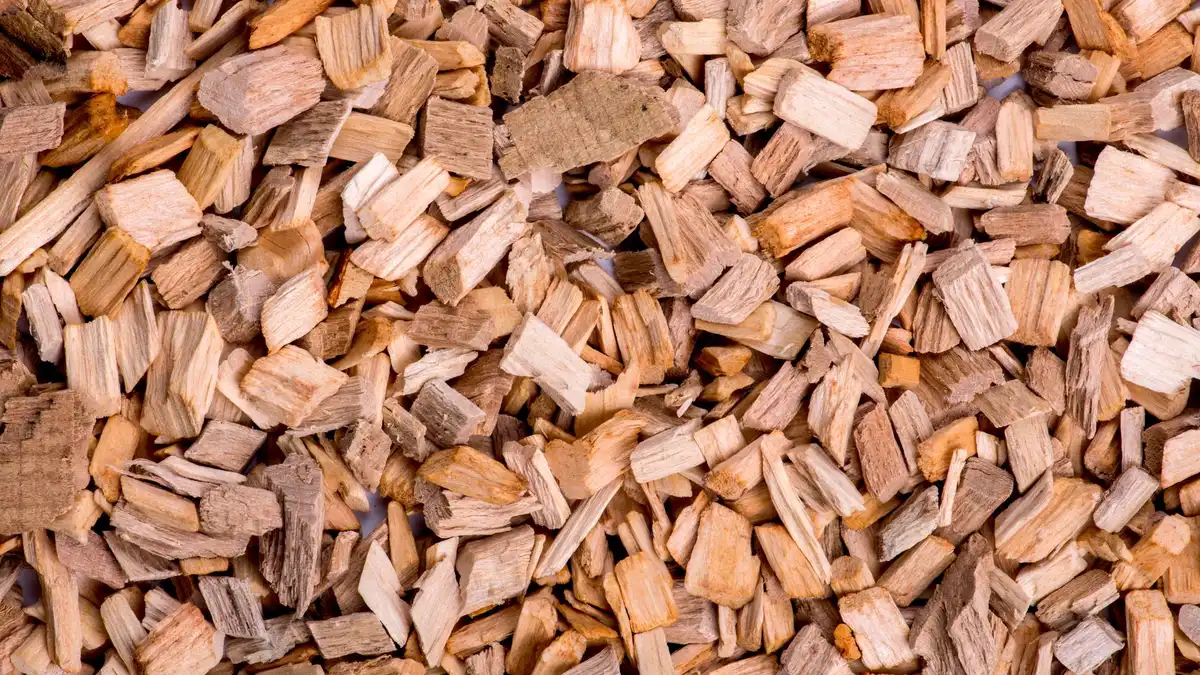 Pilha de lascas de madeira aromática em tons claros e escuros — evoca a matéria-prima do oud e agarwood
