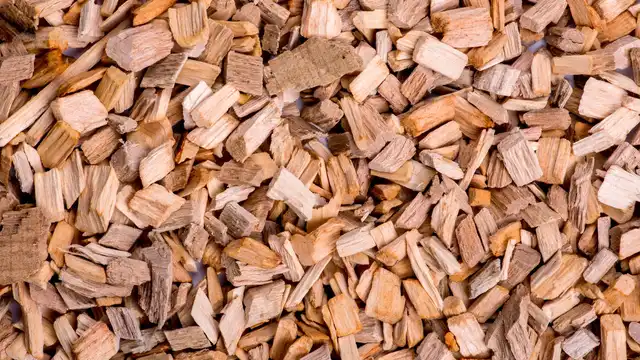 Pilha de lascas de madeira aromática em tons claros e escuros — evoca a matéria-prima do oud e agarwood