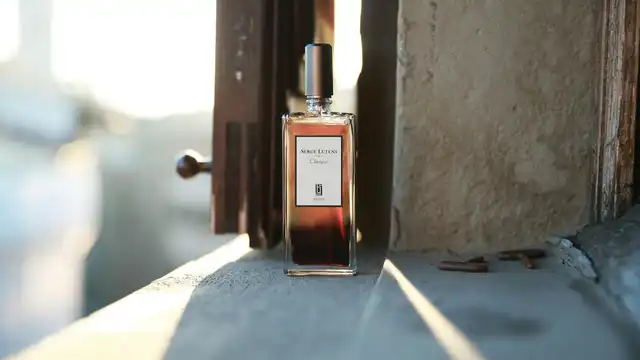 Frasco de perfume âmbar sobre parapeito de pedra com luz dourada de manhã