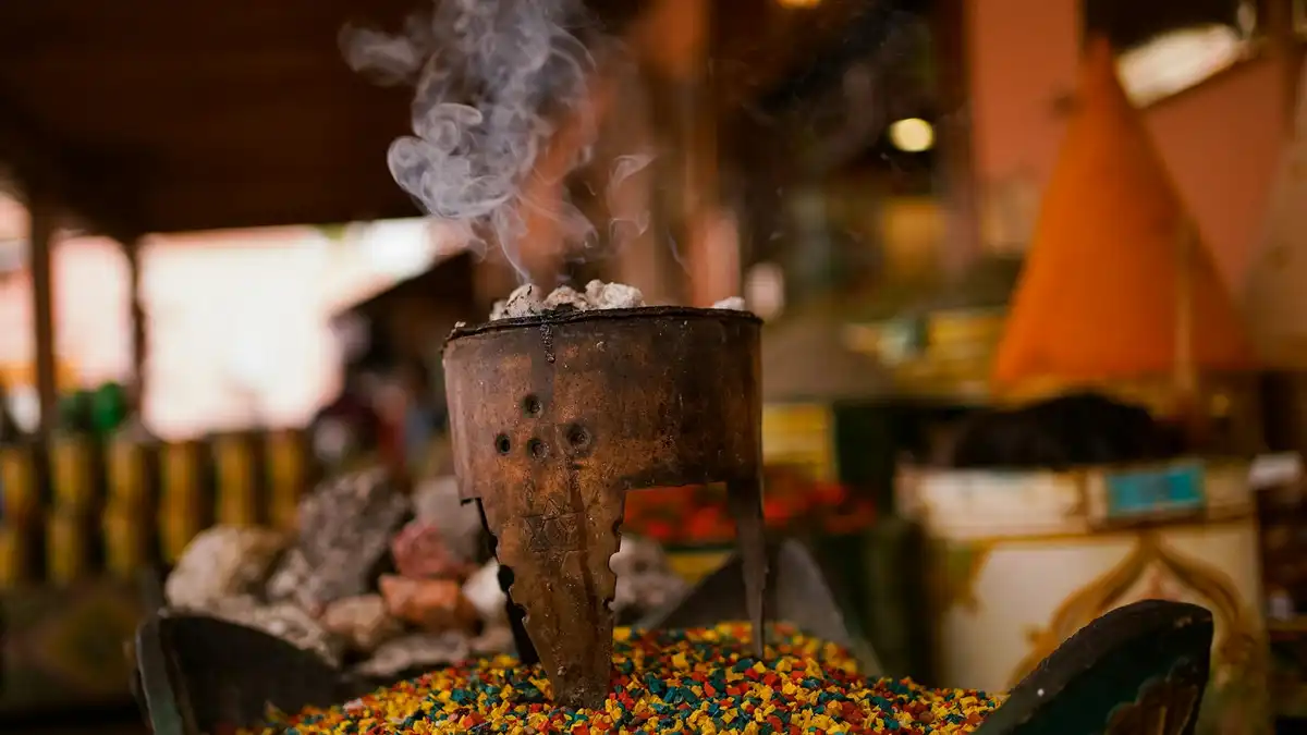 Incensário metálico com resinas coloridas e fumaça subindo em mercado de especiarias — metáfora visual do calor e das resinas dos perfumes orientais masculinos