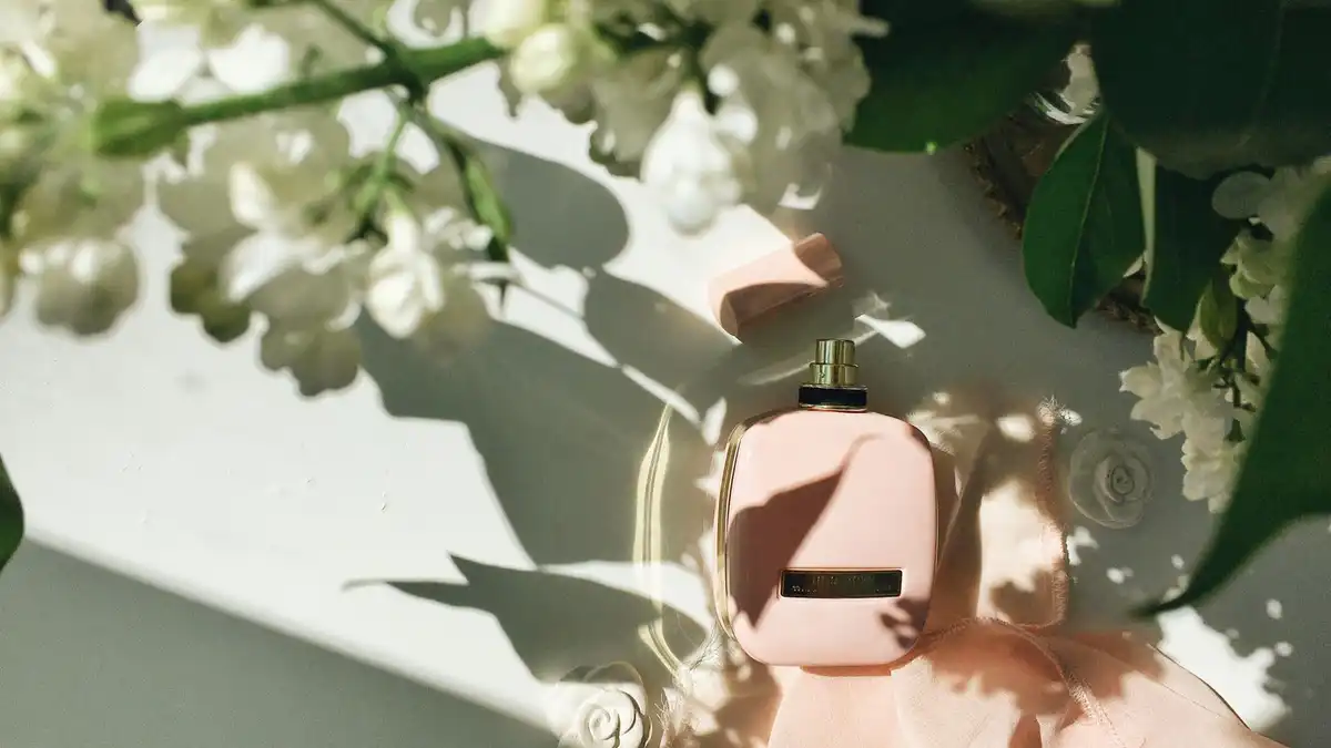 Frasco de perfume feminino rosa com flores brancas e luz suave, evocando elegância noturna