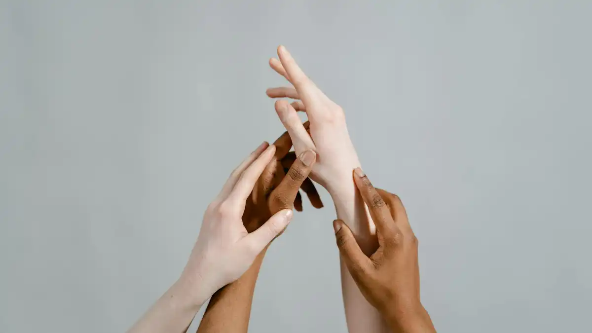 Três mãos com tons de pele diferentes unidas em gesto de conexão sobre fundo neutro