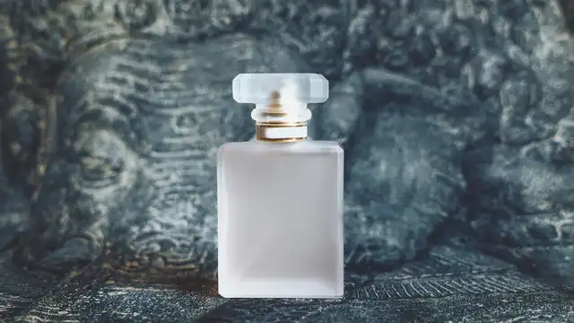 Frasco de perfume de luxo em vidro fosco com detalhes dourados sobre fundo escuro texturizado