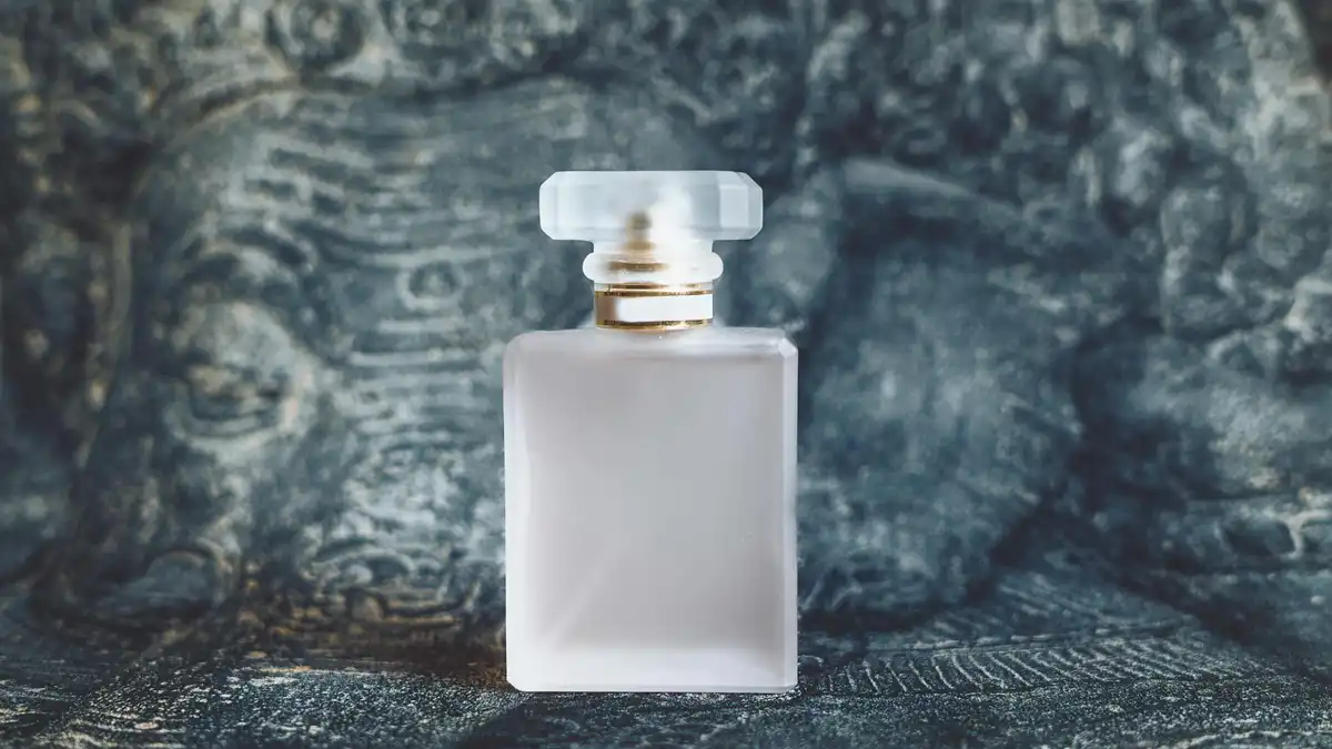 Frasco de perfume de luxo em vidro fosco com detalhes dourados sobre fundo escuro texturizado