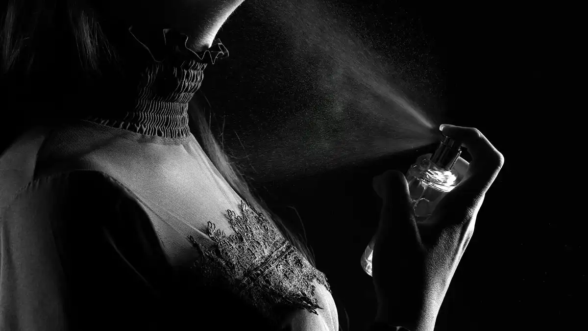 Mulher borrifando perfume no pescoço em foto em preto e branco