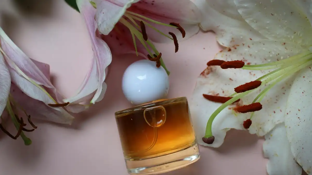 Frasco de perfume âmbar elegante cercado por lírios cor-de-rosa