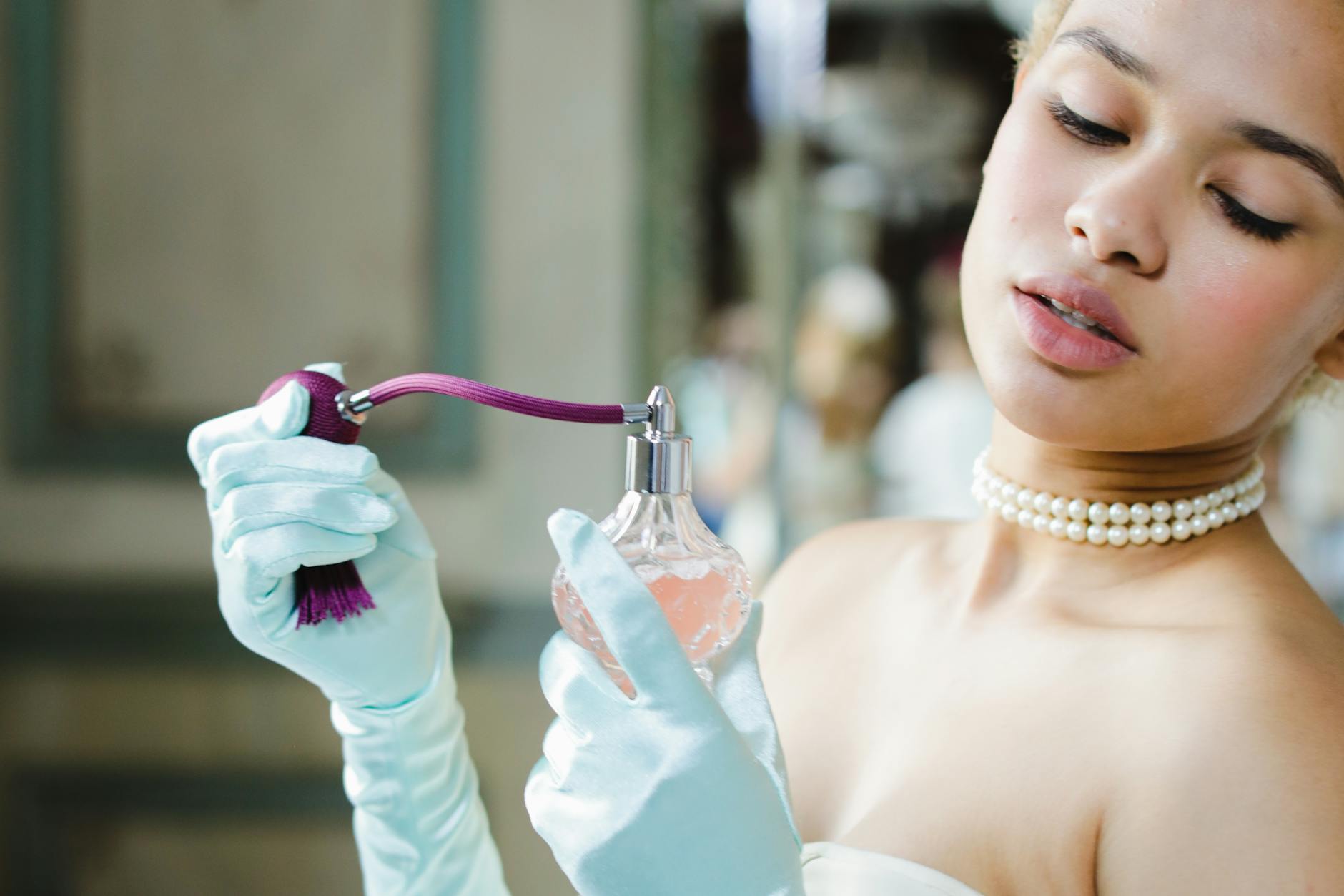 Mulher elegante de luvas segurando um vaporizador de perfume vintage prestes a aplicá-lo