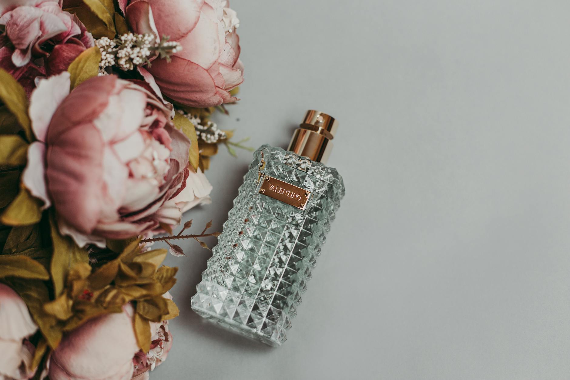 Frasco de perfume facetado ao lado de peônias cor-de-rosa, representando as notas florais de uma fragrância