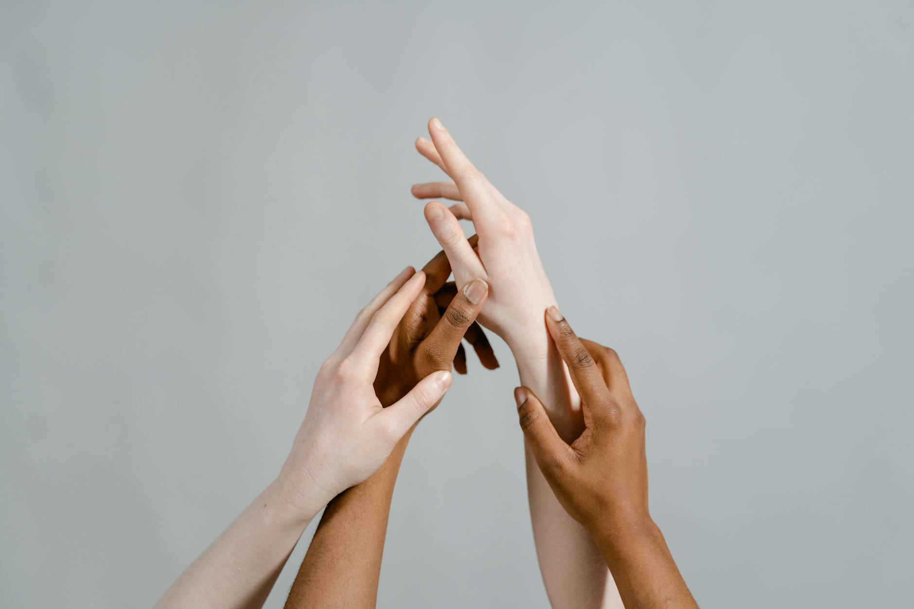 Três mãos com tons de pele diferentes unidas em gesto de conexão sobre fundo neutro