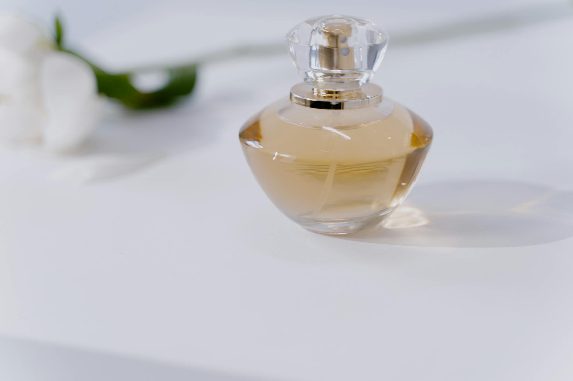 Frasco de perfume feminino dourado com tampa de cristal sobre superfície clara com flores brancas
