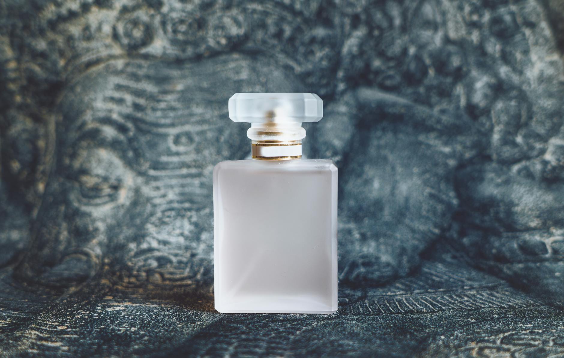 Frasco de perfume de luxo em vidro fosco com detalhes dourados sobre fundo escuro texturizado
